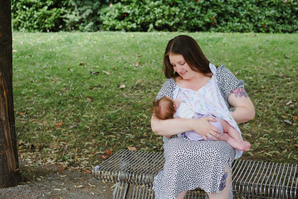 Women breastfeeding her child on a bench in a park