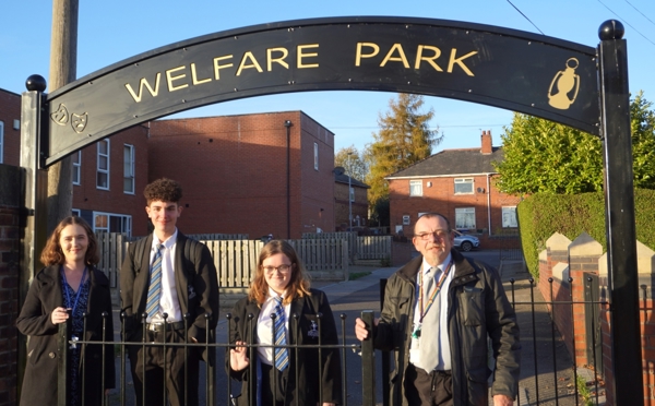 A Group Of People Under A Gateway Reading Welfare Park